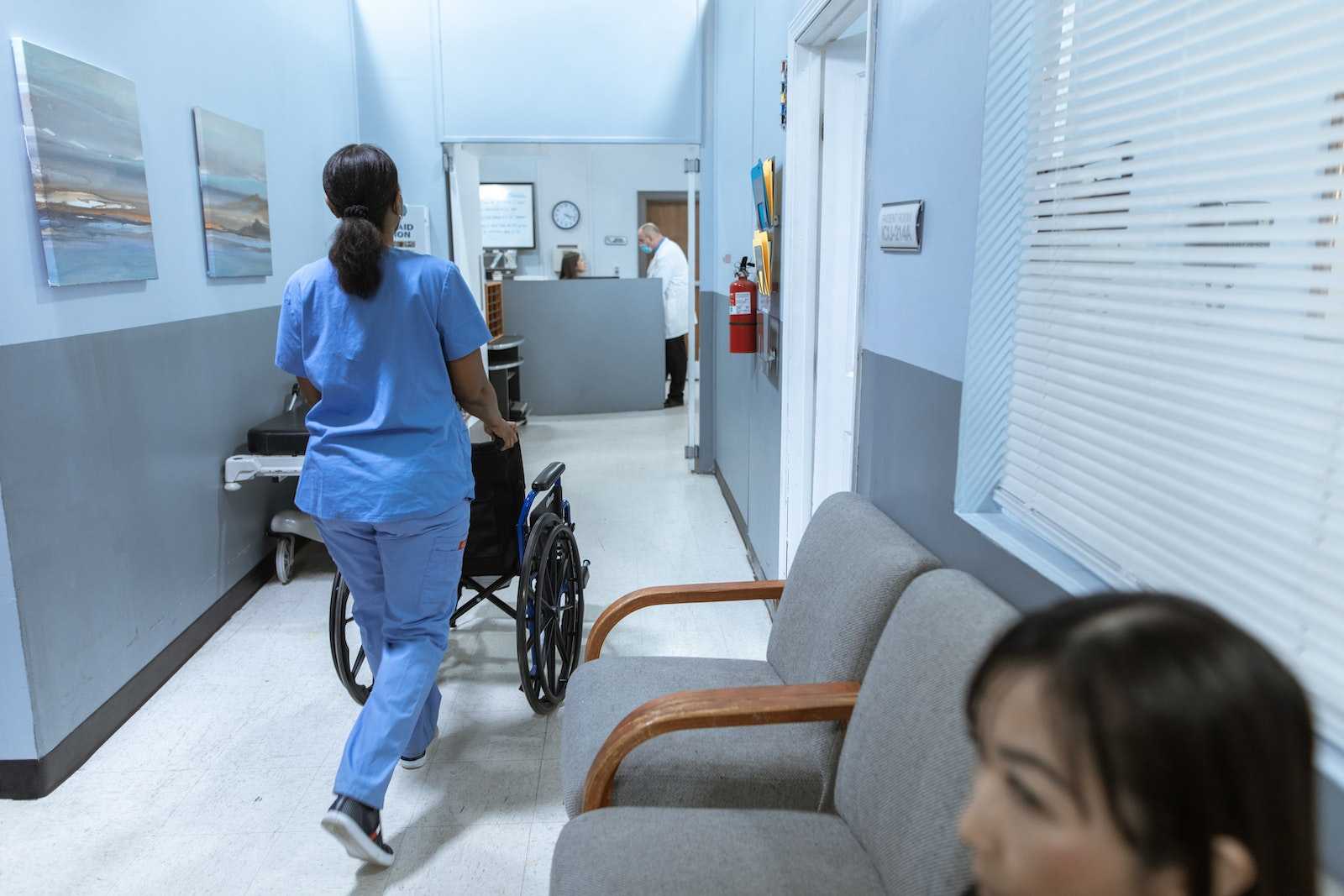 Pielęgniarka pcha wózek inwalidzki na szpitalnym korytarzu